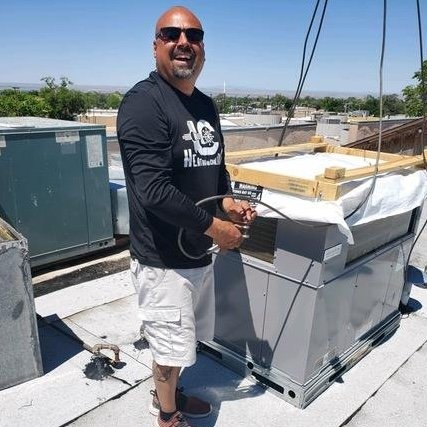 An Air Dynamics of Tulsa technician services an outdoor compressor unit beside a house in Tulsa.